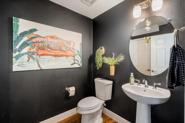 bathroom with toilet, baseboards, visible vents, and wood finished floors