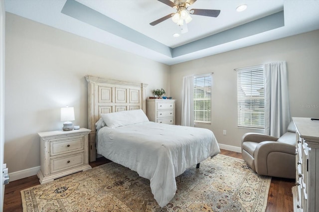 bedroom featuring a tray ceiling, baseboards, and wood finished floors