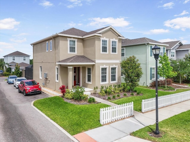 traditional-style home with fence, a shingled roof, a front lawn, and stucco siding