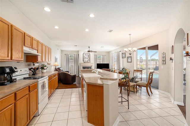 kitchen with white range with electric stovetop, a fireplace, under cabinet range hood, and light tile patterned flooring