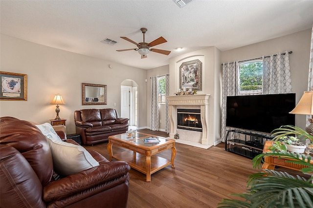 living room with ceiling fan, a fireplace, arched walkways, dark wood finished floors, and visible vents