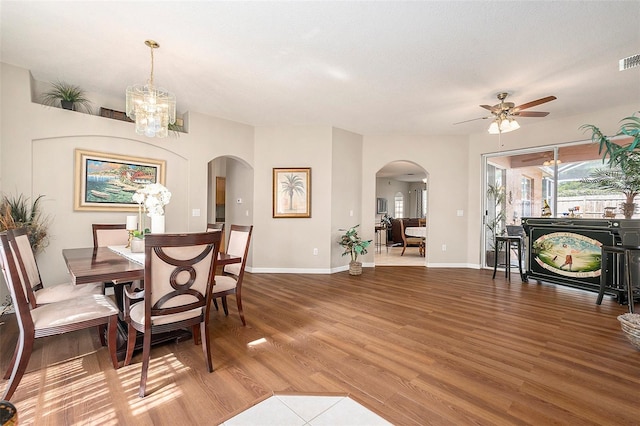 dining room with arched walkways, ceiling fan with notable chandelier, wood finished floors, and visible vents