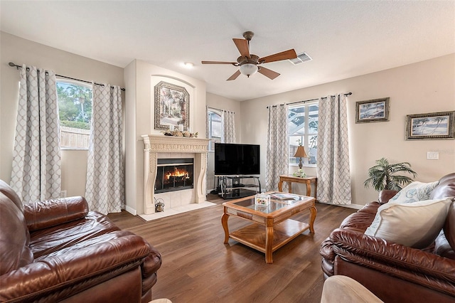 living room with a ceiling fan, visible vents, wood finished floors, a tile fireplace, and baseboards