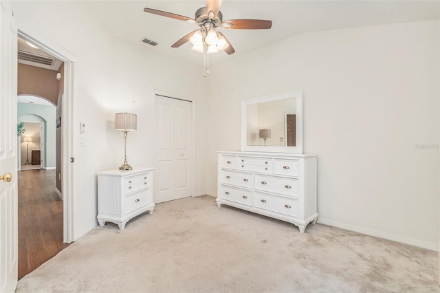 bedroom featuring light colored carpet, arched walkways, lofted ceiling, visible vents, and a closet