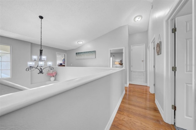 13122 Prestwick Dr, Riverview, FL 33579 - corridor featuring a notable chandelier, baseboards, light wood-type flooring, vaulted ceiling, and a textured ceiling