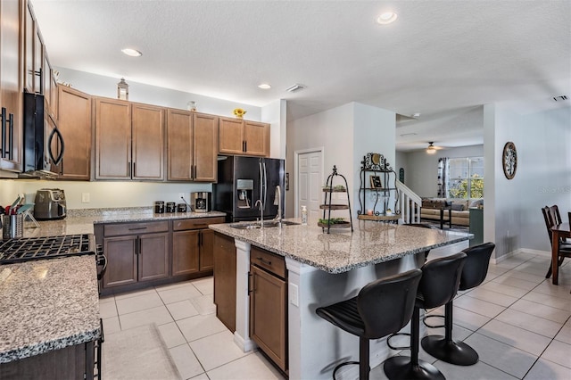8247 Westhaven Dr, Land O Lakes, FL 34638 - kitchen featuring stainless steel microwave, black fridge with ice dispenser, a breakfast bar area, a kitchen island with sink, and light tile patterned floors