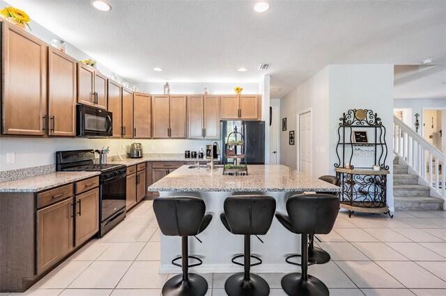 8247 Westhaven Dr, Land O Lakes, FL 34638 - kitchen with black appliances, a breakfast bar area, an island with sink, light stone countertops, and recessed lighting
