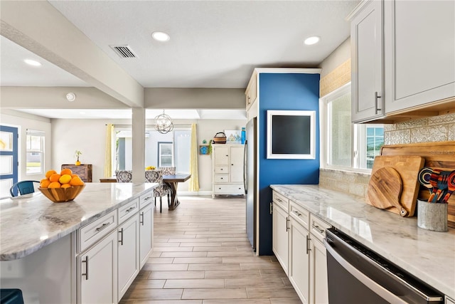 kitchen with white cabinets, visible vents, stainless steel dishwasher, and backsplash