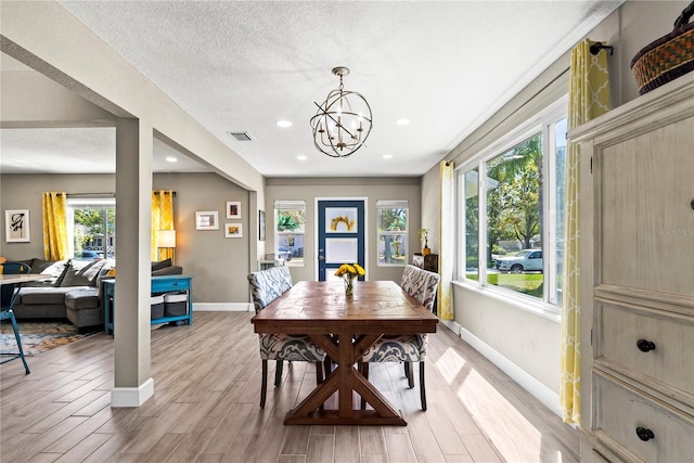 dining area featuring visible vents, baseboards, an inviting chandelier, light wood-style floors, and a textured ceiling