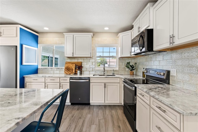 kitchen featuring white cabinetry, black appliances, light stone counters, a sink, and backsplash