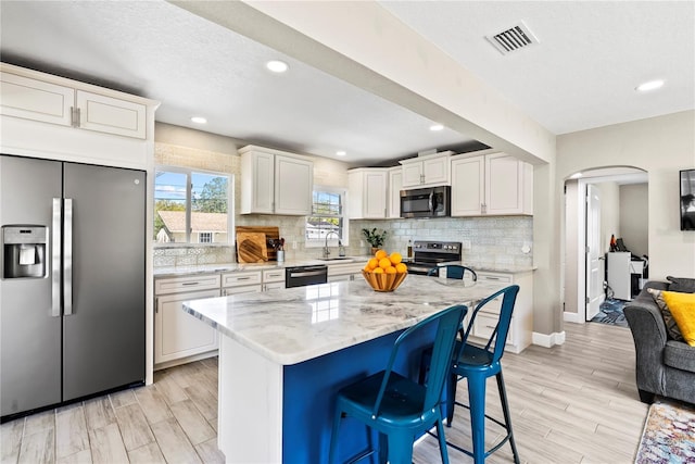 kitchen featuring arched walkways, white cabinetry, appliances with stainless steel finishes, a sink, and decorative backsplash