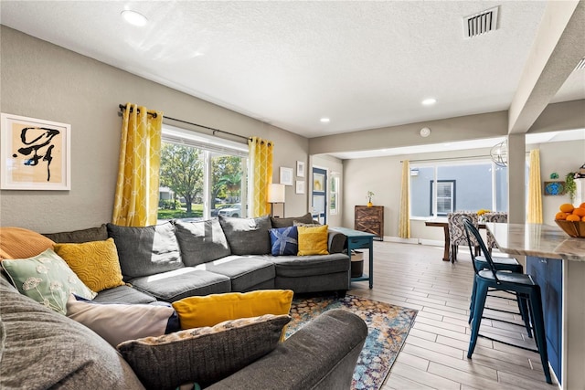 living room featuring visible vents, a textured wall, light wood-style floors, and a textured ceiling