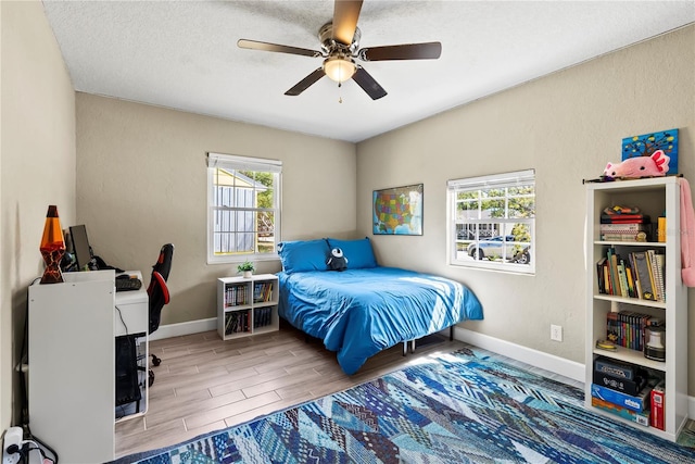 bedroom with a textured ceiling, baseboards, a ceiling fan, and wood tiled floor