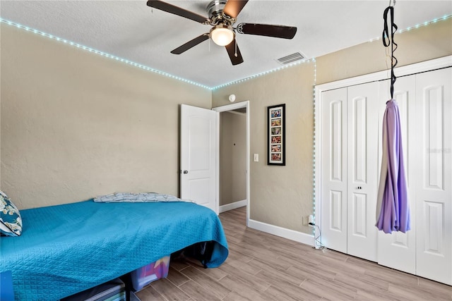 bedroom with a closet, a ceiling fan, visible vents, wood finished floors, and baseboards