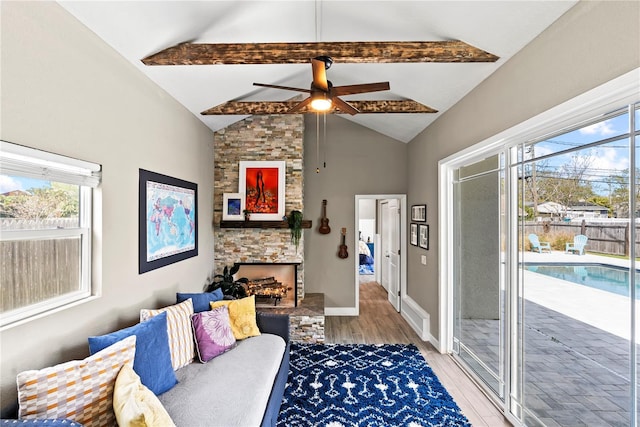 living area featuring a healthy amount of sunlight, light wood-type flooring, a ceiling fan, and lofted ceiling with beams