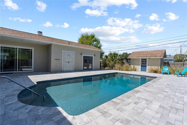 outdoor pool with a patio, a storage structure, fence, and an outbuilding