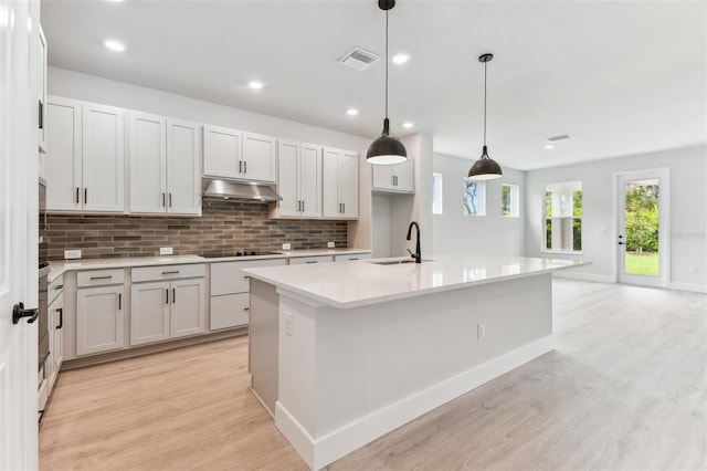 11884 Richmond Trl, Parrish, FL 34219 - kitchen with light wood finished floors, under cabinet range hood, backsplash, a center island with sink, and light countertops