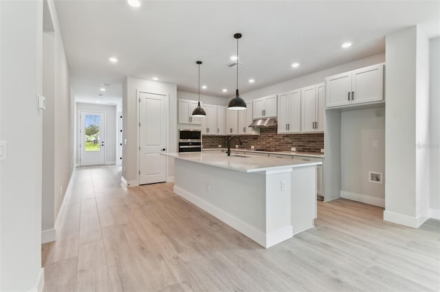 11884 Richmond Trl, Parrish, FL 34219 - kitchen featuring under cabinet range hood, black appliances, decorative backsplash, light wood-style flooring, and an island with sink