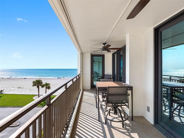 balcony featuring a beach view, a ceiling fan, and a water view