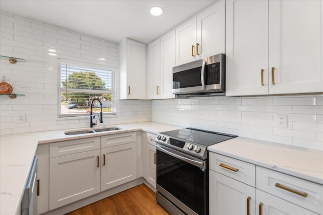 331 Barbara Cir, Belleair, FL 33756 - kitchen with appliances with stainless steel finishes, a sink, white cabinets, light wood-style floors, and decorative backsplash