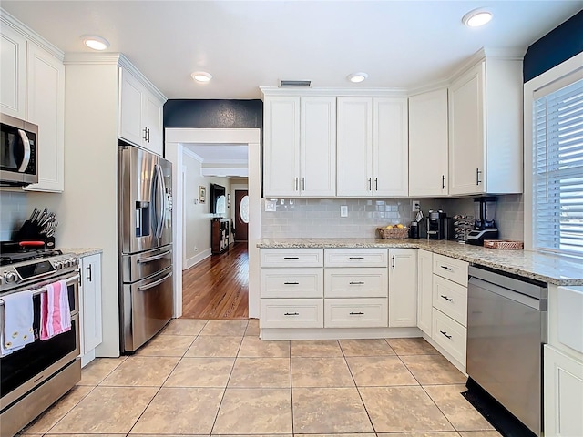 kitchen featuring light tile patterned floors, backsplash, white cabinets, light stone countertops, and appliances with stainless steel finishes