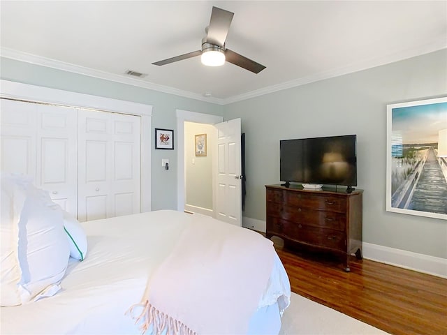 bedroom featuring a closet, visible vents, crown molding, baseboards, and wood finished floors