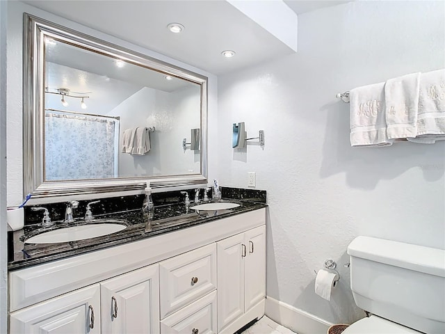 bathroom with double vanity, toilet, baseboards, and a sink