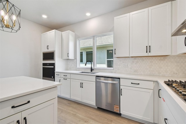 kitchen featuring a sink, light wood-type flooring, white cabinetry, backsplash, and appliances with stainless steel finishes