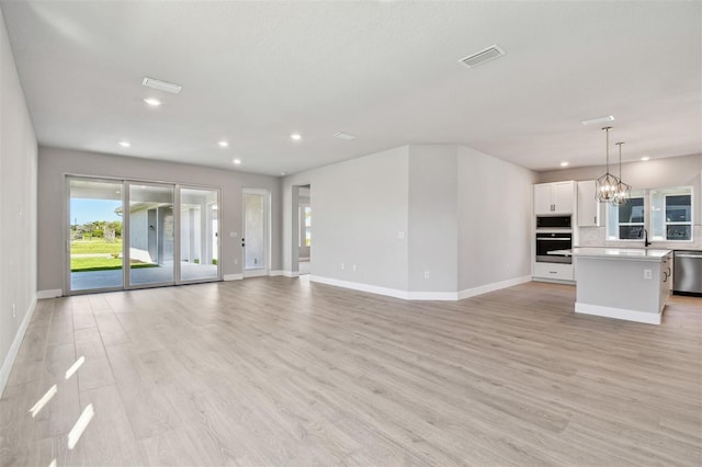 unfurnished living room featuring an inviting chandelier, light wood finished floors, baseboards, visible vents, and recessed lighting
