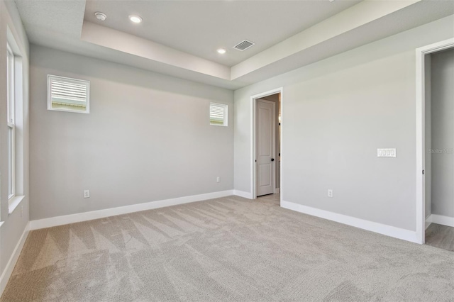 empty room with light colored carpet, baseboards, visible vents, and a raised ceiling