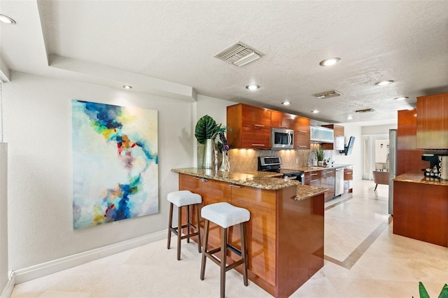 4522 W N B St, Tampa, FL 33609 - kitchen featuring stainless steel appliances, light stone counters, visible vents, a peninsula, and brown cabinetry