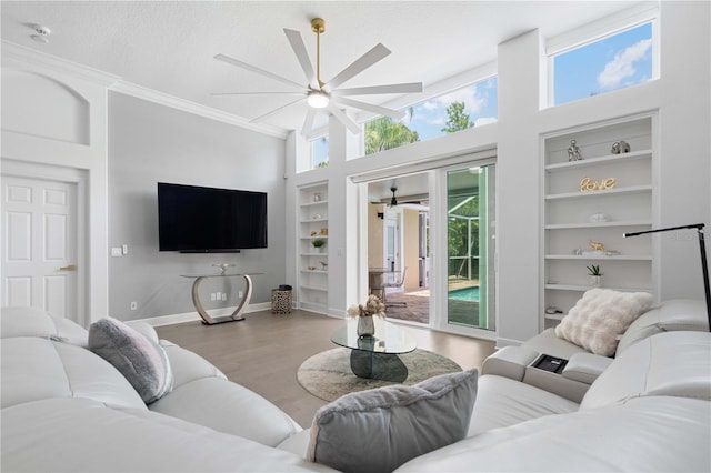 living room featuring crown molding, built in features, a ceiling fan, baseboards, and wood finished floors