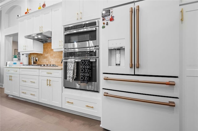 kitchen with tasteful backsplash, light countertops, white cabinets, under cabinet range hood, and stainless steel appliances