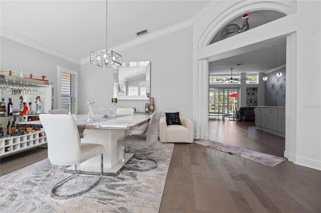 dining space with ceiling fan with notable chandelier, baseboards, wood finished floors, visible vents, and ornamental molding