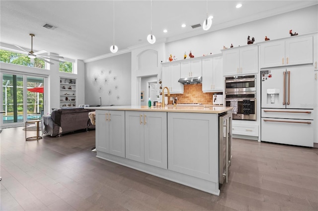 kitchen featuring crown molding, stainless steel double oven, high end white fridge, under cabinet range hood, and visible vents