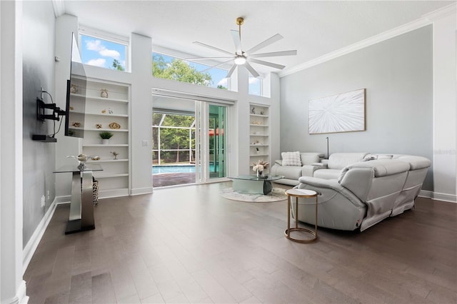 living area with crown molding, built in shelves, a ceiling fan, baseboards, and wood finished floors