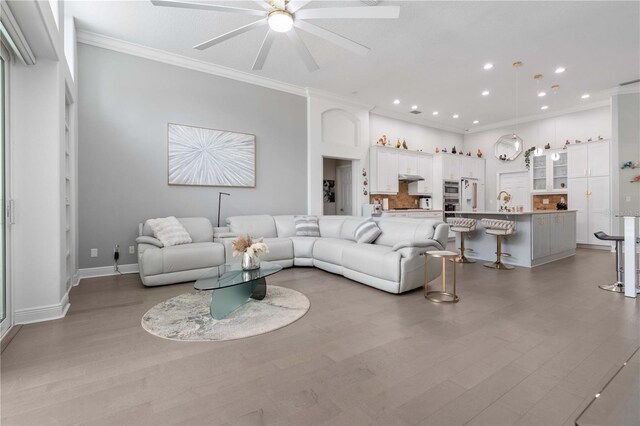 living room featuring ornamental molding, light wood-style floors, baseboards, recessed lighting, and a ceiling fan