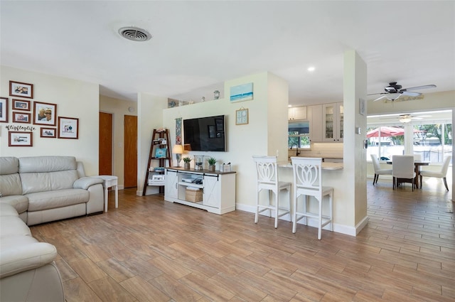 living area with light wood-type flooring, baseboards, ceiling fan, and visible vents