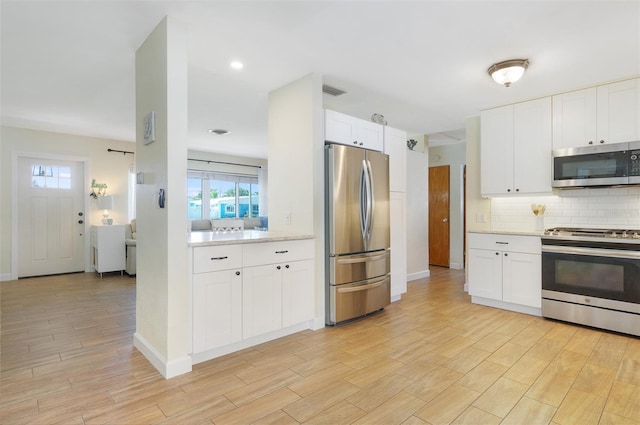 kitchen featuring white cabinetry, light countertops, light wood-type flooring, stainless steel appliances, and decorative backsplash