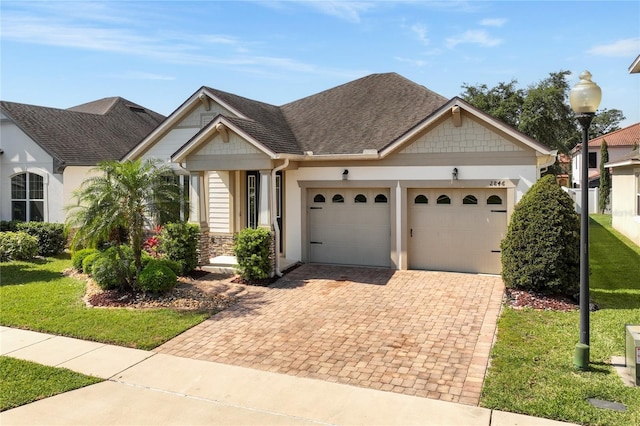 ranch-style home featuring decorative driveway, stone siding, a front lawn, an attached garage, and a shingled roof