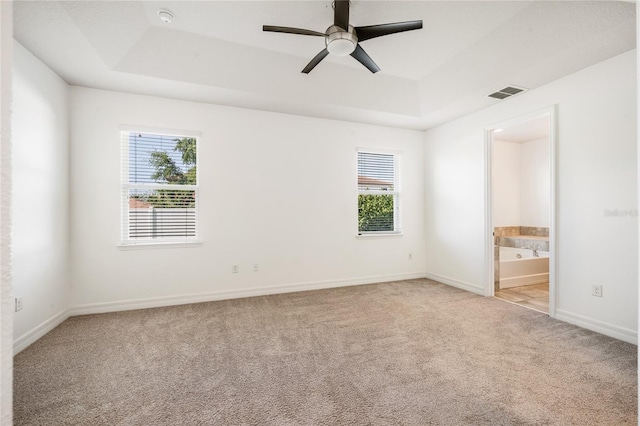 unfurnished bedroom featuring baseboards, light carpet, ensuite bathroom, visible vents, and a tray ceiling