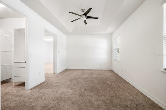 unfurnished bedroom with a spacious closet, carpet flooring, ceiling fan, and a raised ceiling
