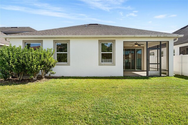 rear view of property featuring a shingled roof, a sunroom, a lawn, fence, and stucco siding