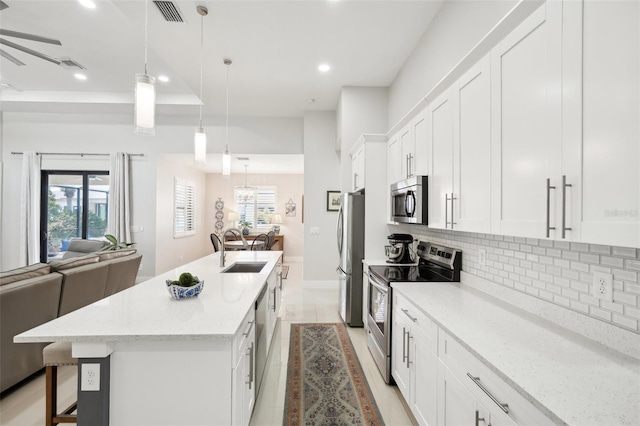 kitchen featuring open floor plan, a breakfast bar area, decorative backsplash, a sink, and appliances with stainless steel finishes