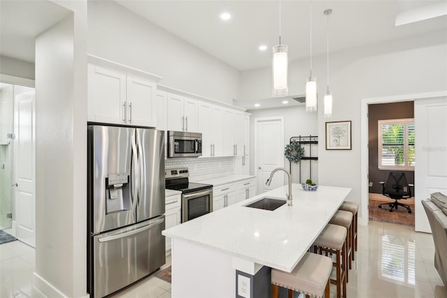 kitchen featuring stainless steel appliances, white cabinetry, a sink, a breakfast bar area, and backsplash