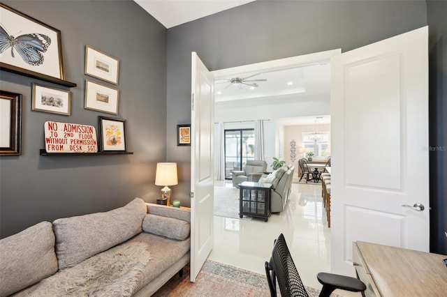 living area featuring a tray ceiling and ceiling fan with notable chandelier