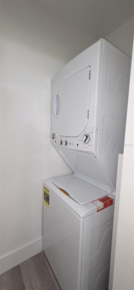 laundry area featuring baseboards, wood finished floors, stacked washer / dryer, and laundry area
