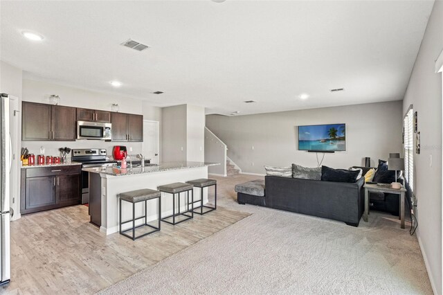 12856 French Market Dr, Riverview, FL 33579 - kitchen with open floor plan, a breakfast bar, visible vents, dark brown cabinets, and appliances with stainless steel finishes