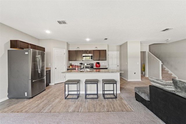 12856 French Market Dr, Riverview, FL 33579 - kitchen with dark brown cabinetry, a breakfast bar area, appliances with stainless steel finishes, a center island with sink, and visible vents