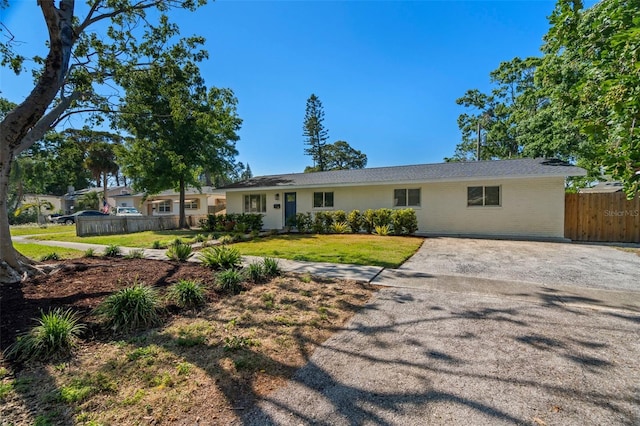 ranch-style house with driveway, fence, and a front lawn